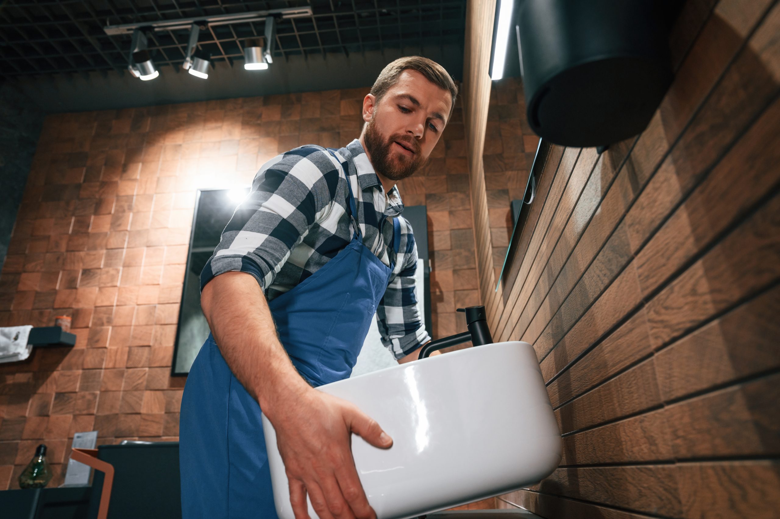 Holding and moving a sink. Plumber in blue uniform is at work in the bathroom