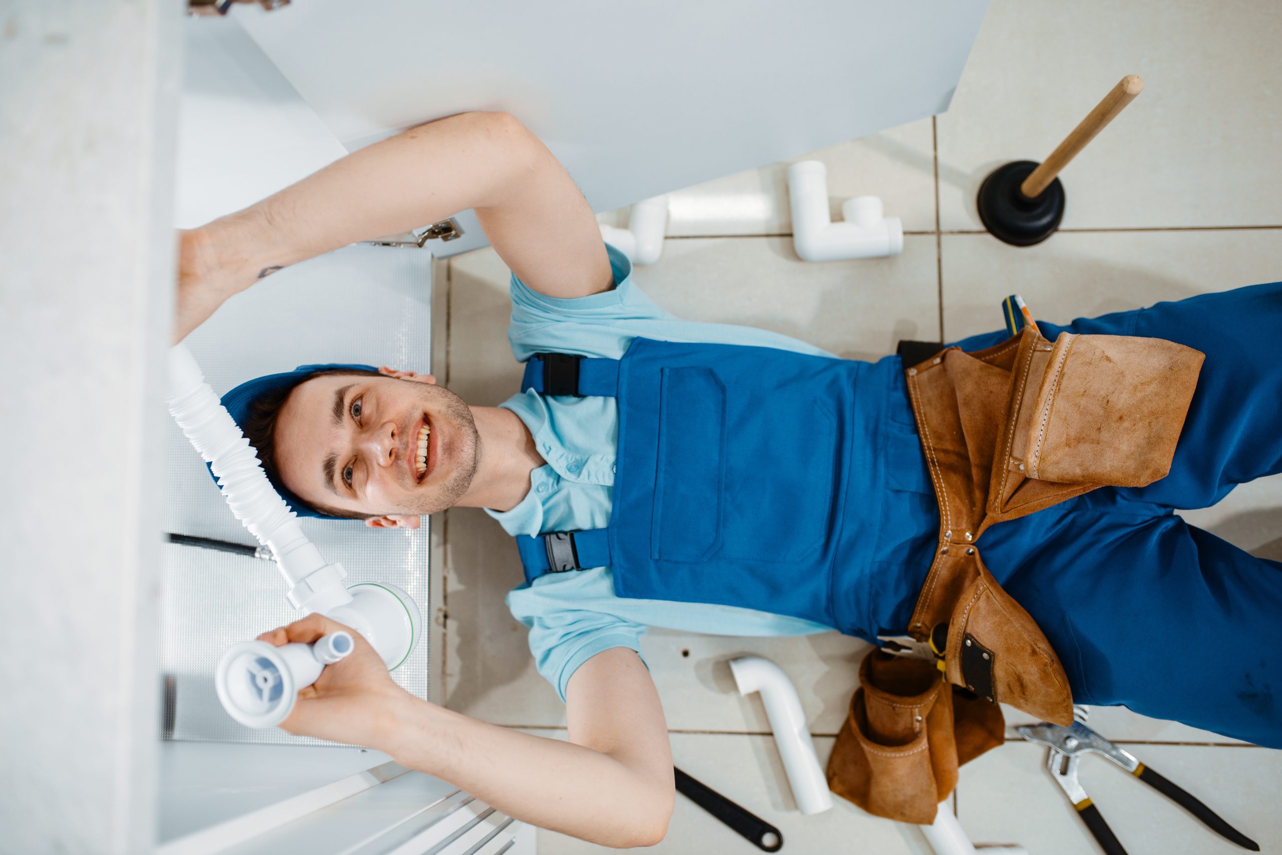 Plumber in uniform installing drain pipe, top view